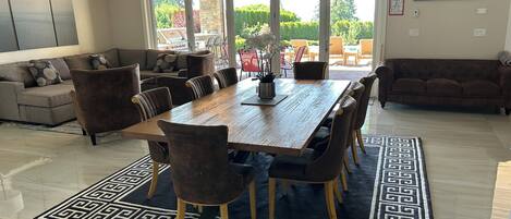 A spacious dining area with a large wooden table and matching chairs, a patterned rug, and a view of the outdoors through large sliding doors.