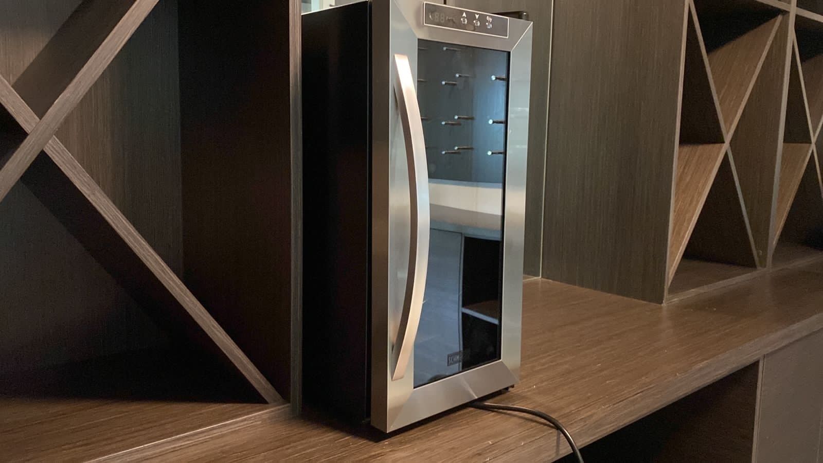 Eine moderne, metallische Verkaufsmaschine mit Glastür, auf einer Holzauskładung mit geometrischen Regalen platziert.
