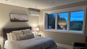 Un dormitorio con una cama grande, una mesita de noche, una lámpara, una ventana con vistas y un cuadro en la pared.