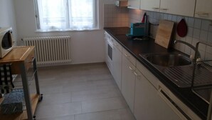 A kitchen with white cabinets, a black countertop, a built-in oven, a microwave, and a window with white curtains. - Simona Fontile 11 by Interhome (Minusio)