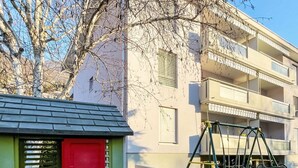 A children's playhouse with a ladder, a swing set, and a building in the background. - Simona Fontile 11 by Interhome (Minusio)