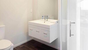 Un baño moderno con tocador blanco, un espejo grande y cabina de ducha de vidrio.