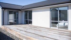 Una casa moderna con terraza de madera, grandes puertas correderas de vidrio y techo de metal.