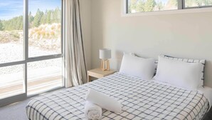 Habitación de hotel con una cama grande, una mesita de noche, una lámpara y vistas a la playa.