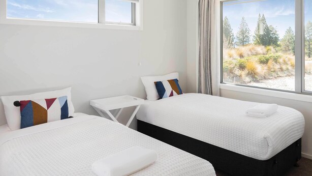 Habitación de hotel con dos camas, una mesita pequeña y ventana con vistas a árboles y arbustos.