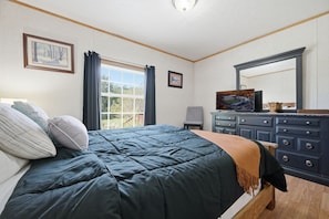 Ein Schlafzimmer mit Bett, Kommode, Fernseher und einem Fenster mit Vorhängen.