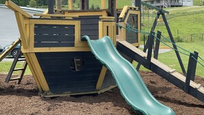 Une aire de jeux avec un toboggan, une zone d’escalade et une petite structure en forme de bâtiment.