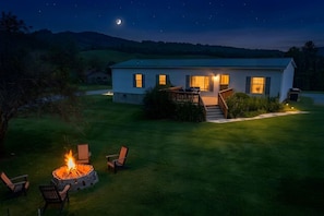 Ein Haus mit Feuerstelle und Gartenmöbeln im Hof, einer Terrasse und einem Mond am Himmel.