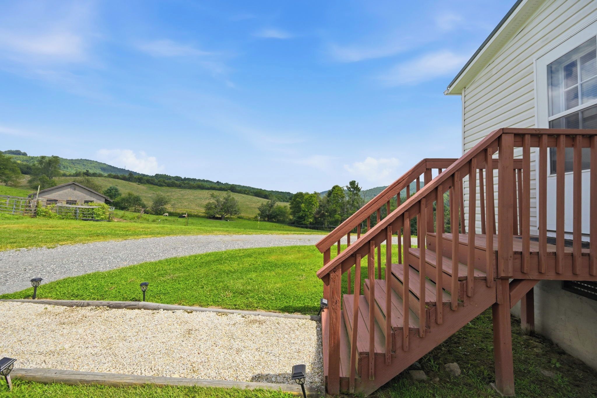 Eine Holztreppe führt zu einem Haus mit einem Schotterweg und einem Bauernhof im Hintergrund.