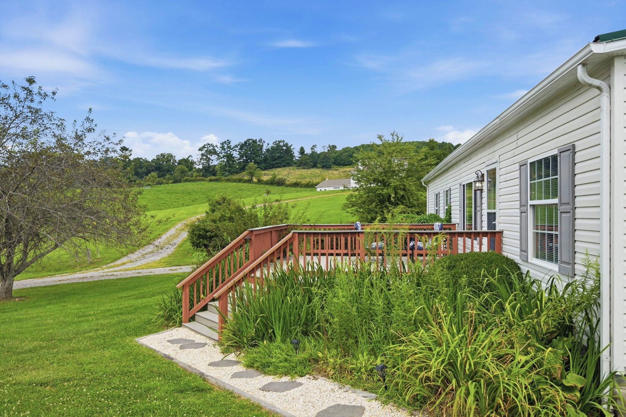 A house with a wooden deck and a gravel pathway leading to a white building.