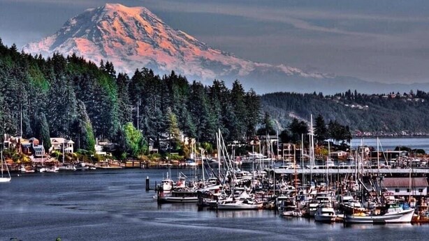 A marina with boats docked, a mountain in the background, and a forested area. - Gig Harbor Downtown Waterfront Retreat (Gig Harbor)
