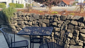 A patio with a stone wall, a metal table, and two chairs. - Gig Harbor Downtown Waterfront Retreat (Gig Harbor)