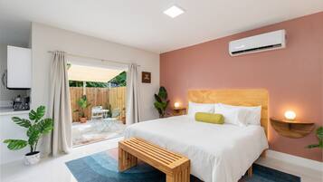 Une chambre à coucher comprenant un lit, des tables de chevet, un climatiseur et donnant sur un espace extérieur.