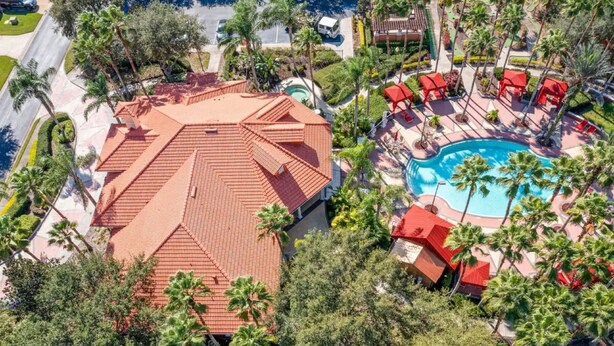 Vista aérea de un resort con piscina, edificios de techo rojo y palmeras.