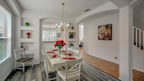 Un comedor con una mesa blanca dispuesta para cuatro personas, una araña y un cuadro en la pared.