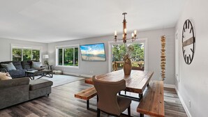 A spacious living room with a large wooden dining table, a comfortable sofa, and a modern chandelier. - Lake Living on Castle Rock Lake, Close to WI Dells, Family Friendly (Mauston)