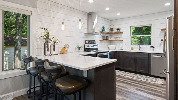 A modern kitchen with a central island, bar stools, a built-in oven, and a window overlooking greenery. - Lake Living on Castle Rock Lake, Close to WI Dells, Family Friendly (Mauston)