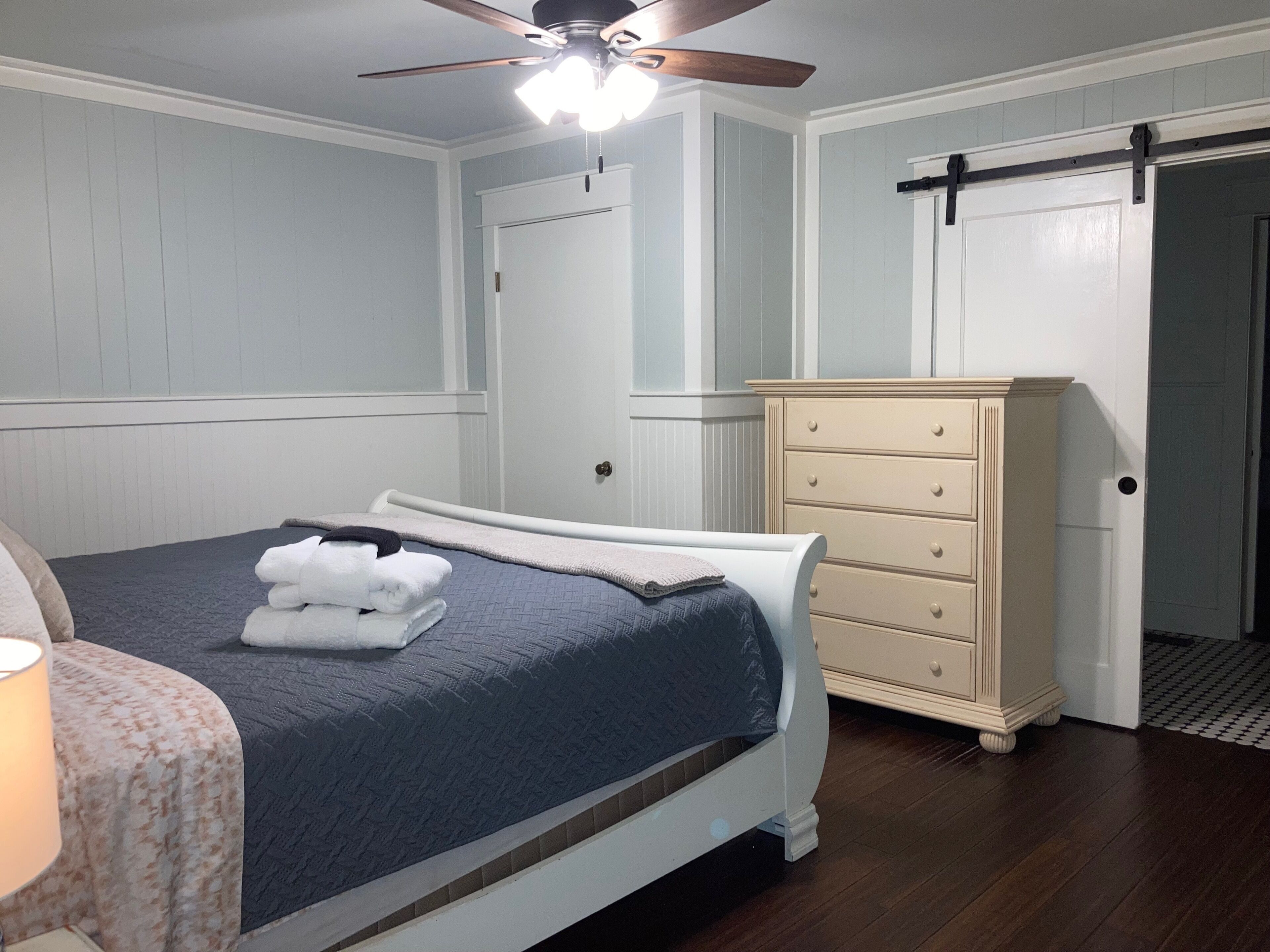 A bedroom with a bed, a dresser, a ceiling fan, and a door.
