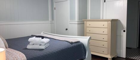 A bedroom with a bed, a dresser, a ceiling fan, and a door.