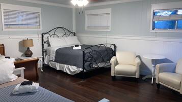 A bedroom with a bed, two chairs, a small table, a lamp, and a ceiling fan.