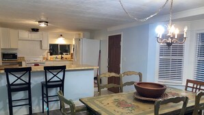 Ein Essbereich mit Tisch, Stühlen, einer Chandelüster und einer Küche im Hintergrund.