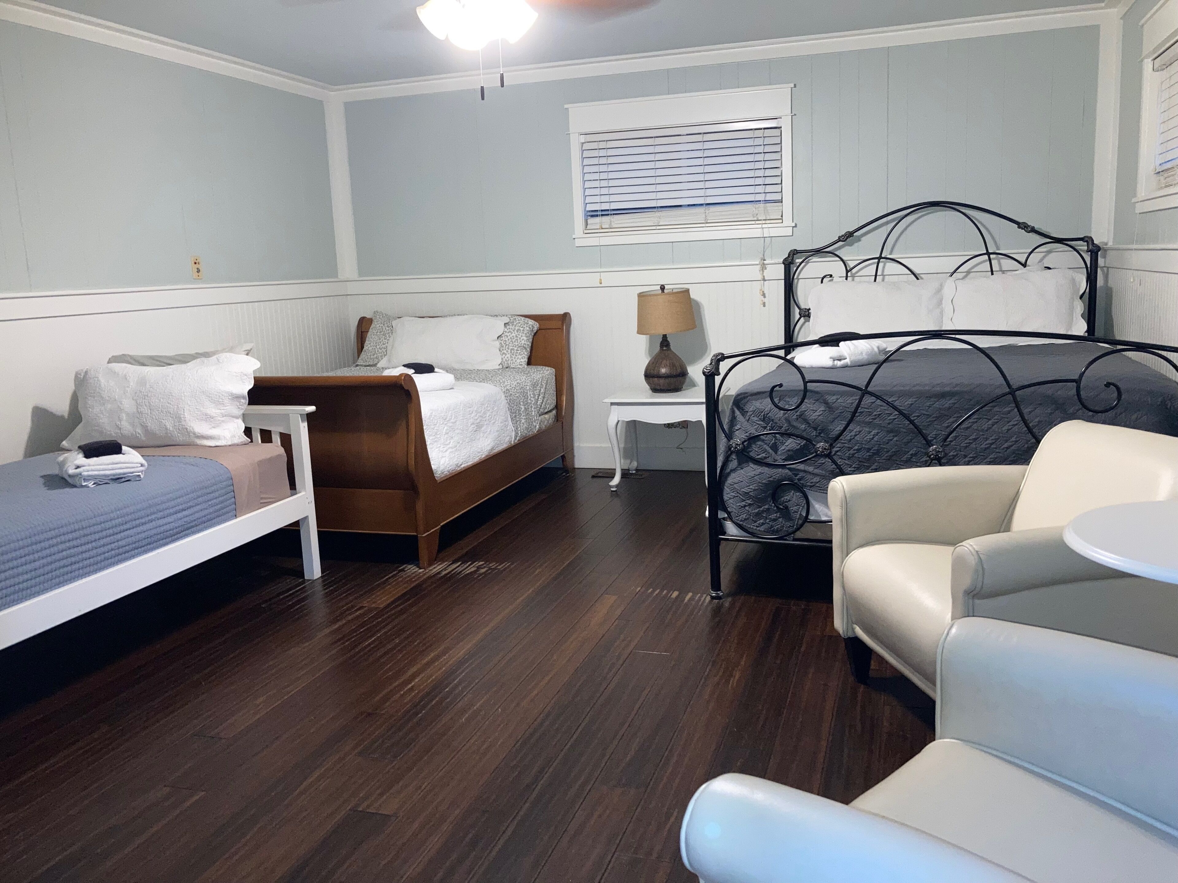 A bedroom with a wooden bed, a smaller bed, a chair, a nightstand, and a lamp.