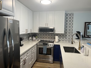 A modern kitchen with white cabinets, a stainless steel refrigerator, a microwave, an oven, and a gas stove.
