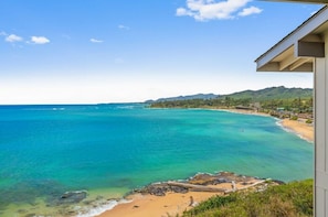 A coastal view with a beach, clear blue waters, and a mountainous backdrop.