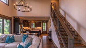 A spacious living area with a large sofa, a chandelier, and a staircase leading to an upper floor. - MountainAire at Eagles Nest -  Views, firepit, gas fire table, Eagles Nest amenities! (Banner Elk)