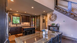A modern kitchen with dark wood cabinets, a large island, and a dining area with a glass table. - MountainAire at Eagles Nest -  Views, firepit, gas fire table, Eagles Nest amenities! (Banner Elk)