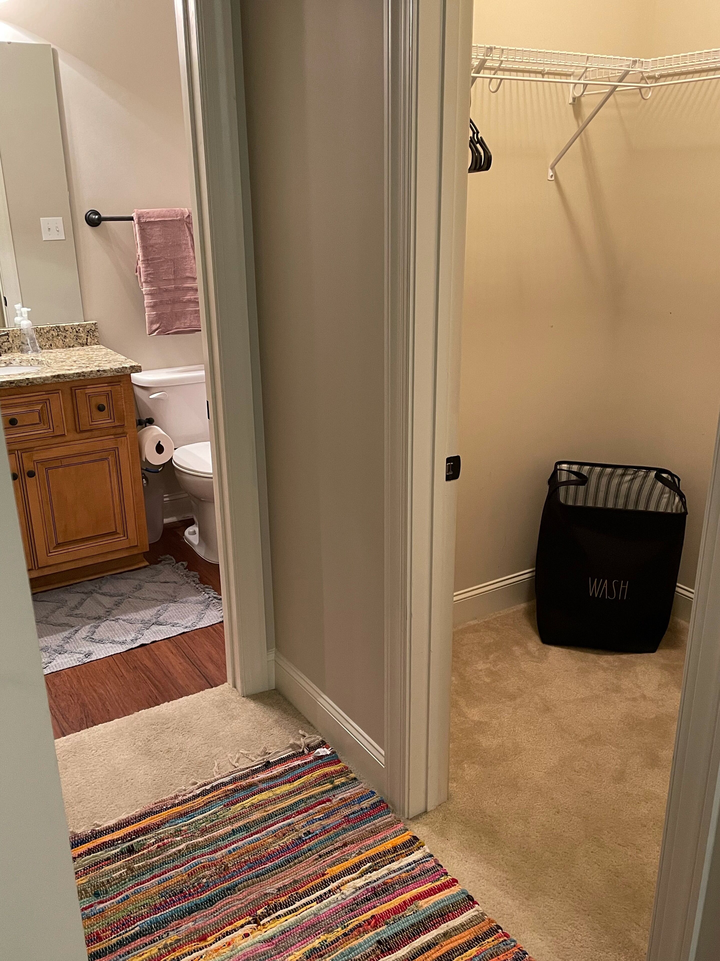 A bathroom with a toilet, a towel rack, a wooden cabinet, and a colorful striped rug.