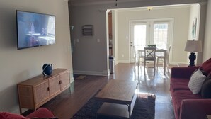 Una sala de estar con una televisión de pantalla plana, un mueble de madera, un sofá rojo, una mesa de centro y una zona de comedor con una mesa y sillas.