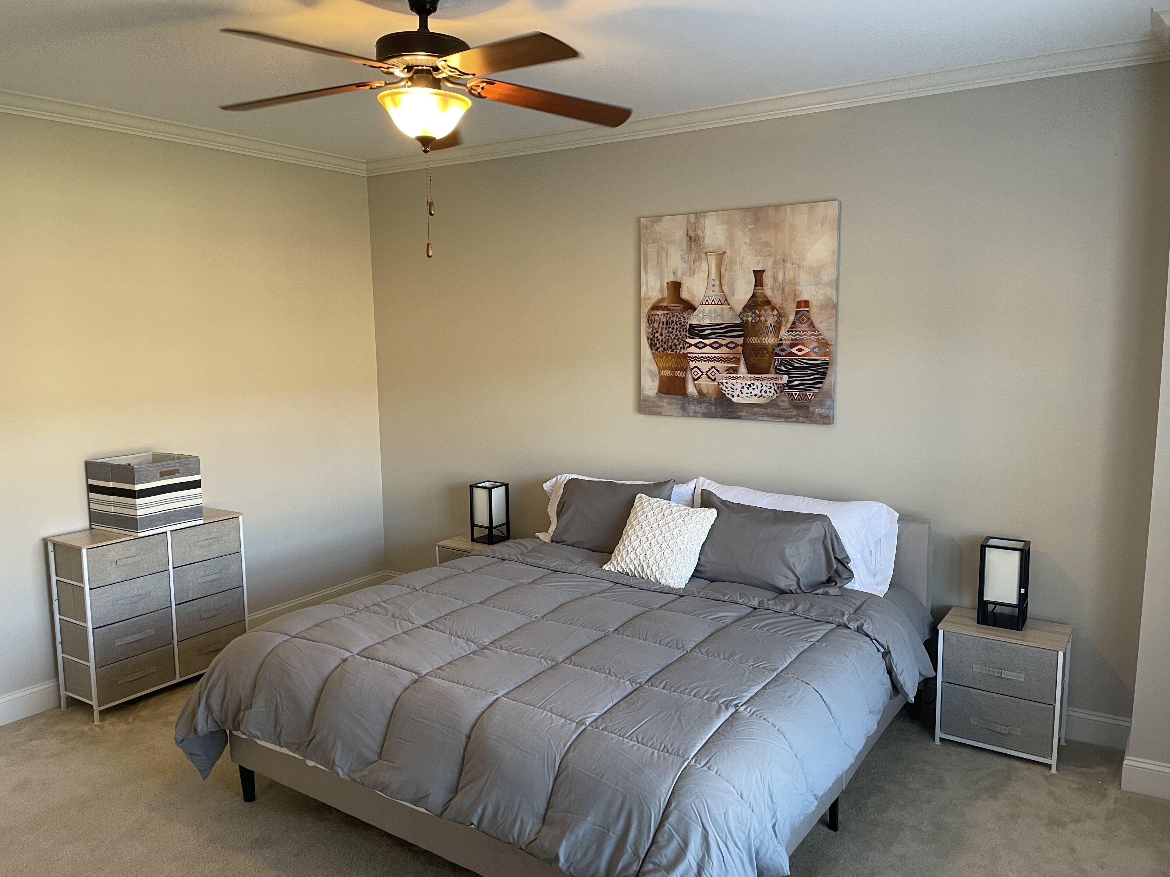 A bedroom with a bed, nightstands, a ceiling fan, and a wall-mounted artwork.