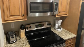 Una cocina con armarios de madera, microondas de acero inoxidable, estufa negra, cafetera y tostadora.