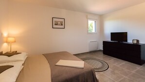 Een slaapkamer met een bed, bedlampje, dressoir, televisie en een lijst aan de muur.