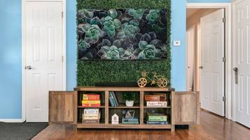 Un couloir avec une console en bois où sont exposés des livres et des jeux, un mur vert orné de plantes succulentes et une porte sur la gauche.