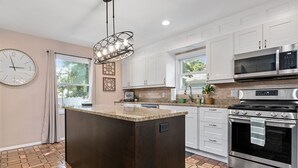 Una cocina moderna con una isla central, electrodomésticos de acero inoxidable y un reloj en la pared.