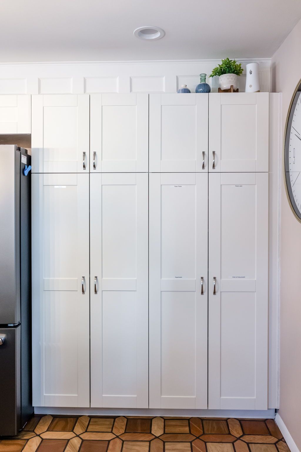 Eine Küche mit weißen Schränken, einem Edelstahlkühlschrank und einer Uhr an der Wand.