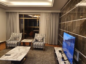 Un saló modern amb dues butaques estampades, una taula de centre de marbre, un televisor sobre un moble i una finestra gran amb cortines.