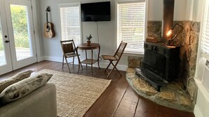 A cozy living room with a stone fireplace, a flat-screen TV, and a guitar. - Private 3 Acre Bungalow (Louisburg)