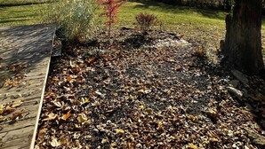 A garden with a wooden deck, a tree, and a clear blue sky. - Private 3 Acre Bungalow (Louisburg)