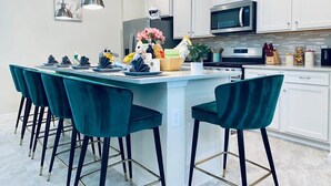A modern kitchen with white cabinets, a central island with bar stools, and a stainless steel microwave. - Delightful Frozen Potter Lake Home Pool Spa Resort (Davenport)