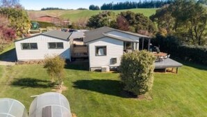 Une maison à deux étages avec un grand jardin devant, une terrasse couverte et un petit espace jardin.