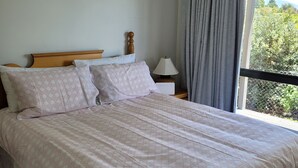 Une chambre à coucher avec un grand lit, une table de chevet, une lampe et une fenêtre avec des rideaux.