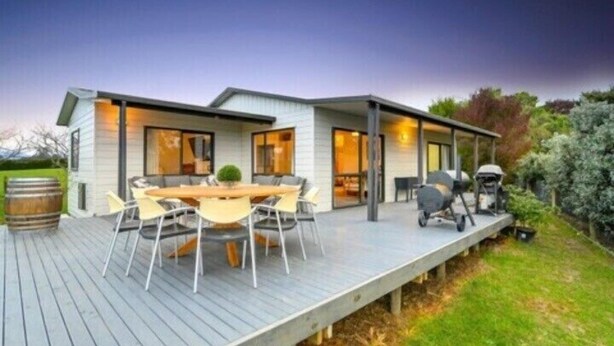Une maison moderne dotée d’une terrasse, d’un espace barbecue et d’une table à manger avec des chaises.