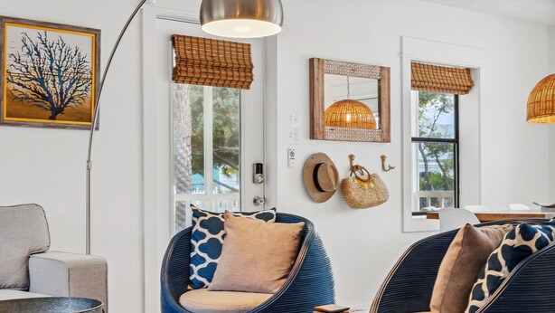 Ein modernes Wohnzimmer mit einer Couch, zwei blauen Sesseln, einem runden Tisch und einem großen Fenster mit Blick ins Freie.