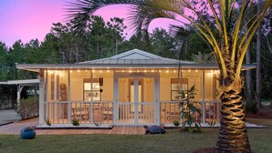 Ein Haus mit überdachter Veranda, einer kleinen Terrasse und einer Palme.