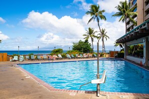Relax by the pool overlooking the ocean, surrounded by palm trees and lounge chairs.