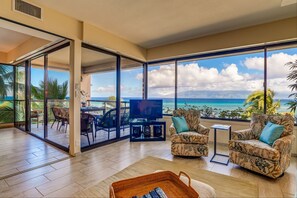 Relax in a spacious living area with a balcony offering breathtaking ocean views and a comfortable seating area.