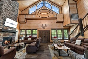 A spacious living room with a stone fireplace, multiple seating areas, and a large wooden ceiling with skylights.